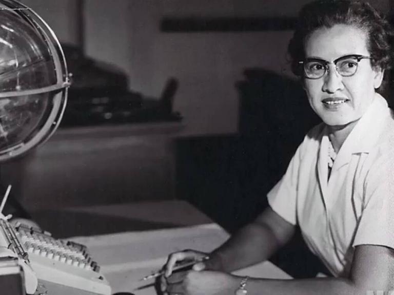 Die Mathematikerin Katherine sitzt an ihrem Schreibtisch, vor ihr eine Schreibmaschine und ein Globus. Schwarz-weiß Bild.
