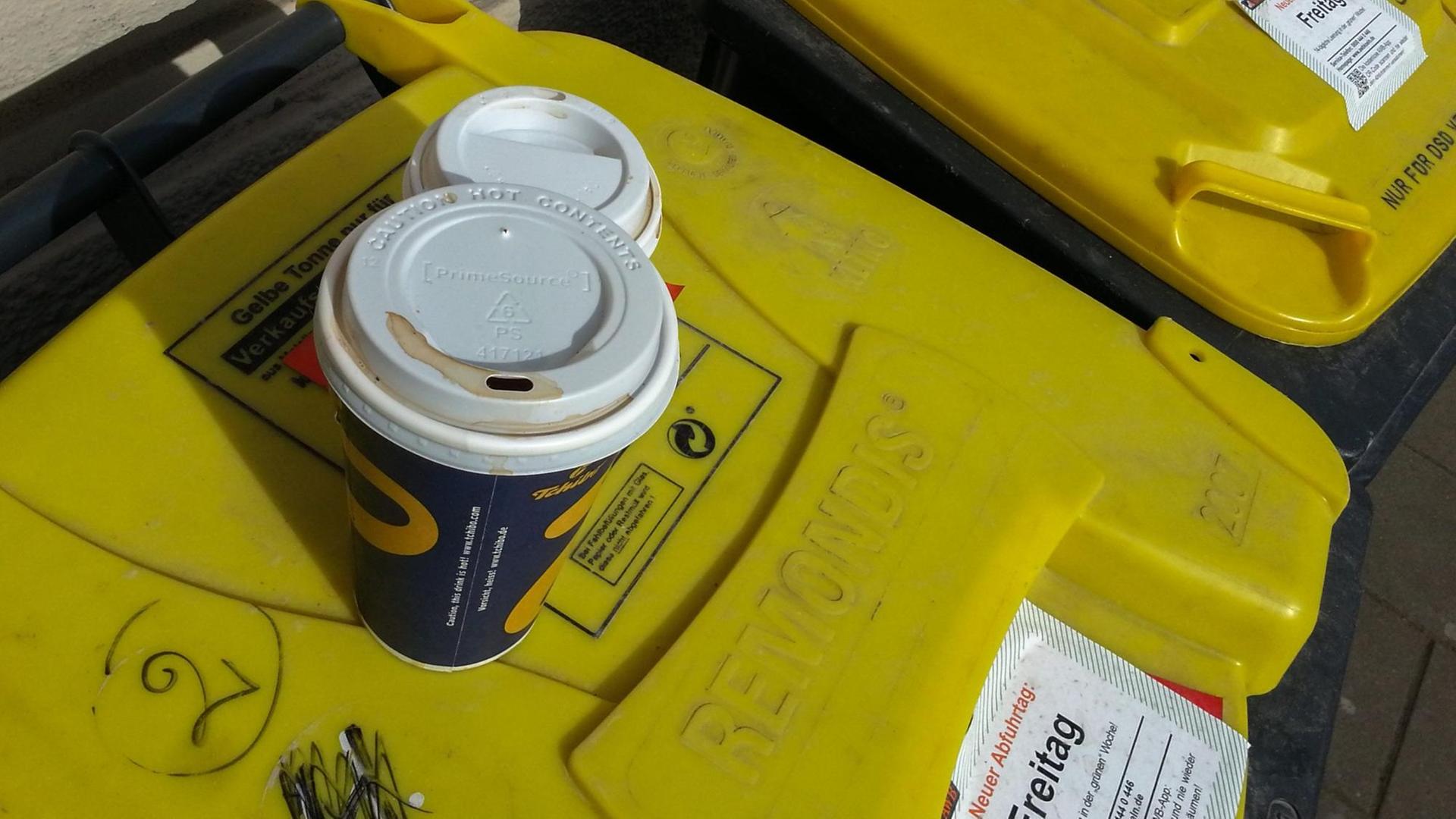 Auf der gelben Tonne für Plastikmüll hat jemand zwei leere Kaffeebecher aus Pappe deponiert. Aufgenommen in Köln.
