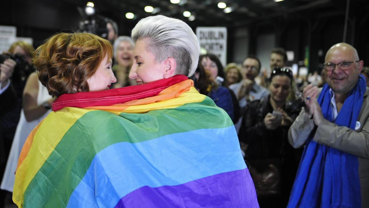 2 Frauen umarmen sich, eingewickelt in eine Regenbogen-Fahne