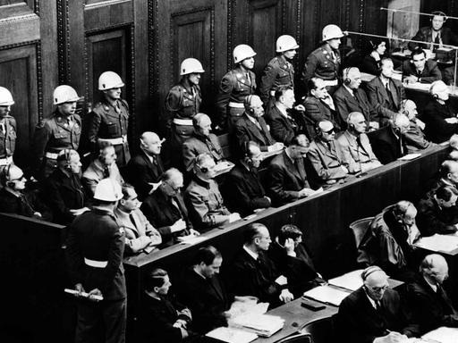 Blick auf die Anklagebank beim Kriegsverbrecherprozess in Nürnberg, 18.03.1946. Die Angeklagten schauen interessiert zum Zeugenstand (nicht im Bild) in dem im Moment dieser Aufnahme gerade Hermann Göring saß und seine Aussage machte.