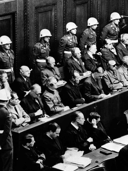 Blick auf die Anklagebank beim Kriegsverbrecherprozess in Nürnberg, 18.03.1946. Die Angeklagten schauen interessiert zum Zeugenstand (nicht im Bild) in dem im Moment dieser Aufnahme gerade Hermann Göring saß und seine Aussage machte.