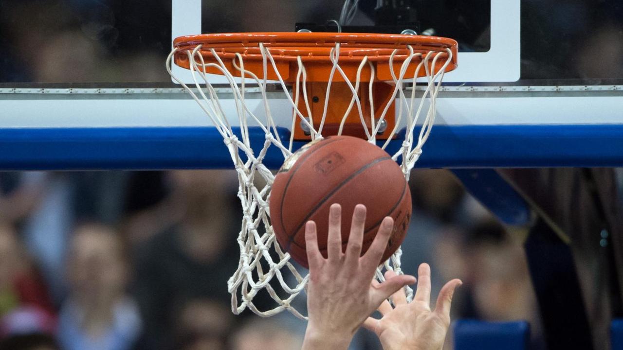 Hände recken sich unter einem Basketballkorb nach dem Ball.