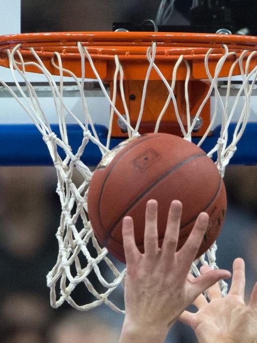 Hände recken sich unter einem Basketballkorb nach dem Ball.