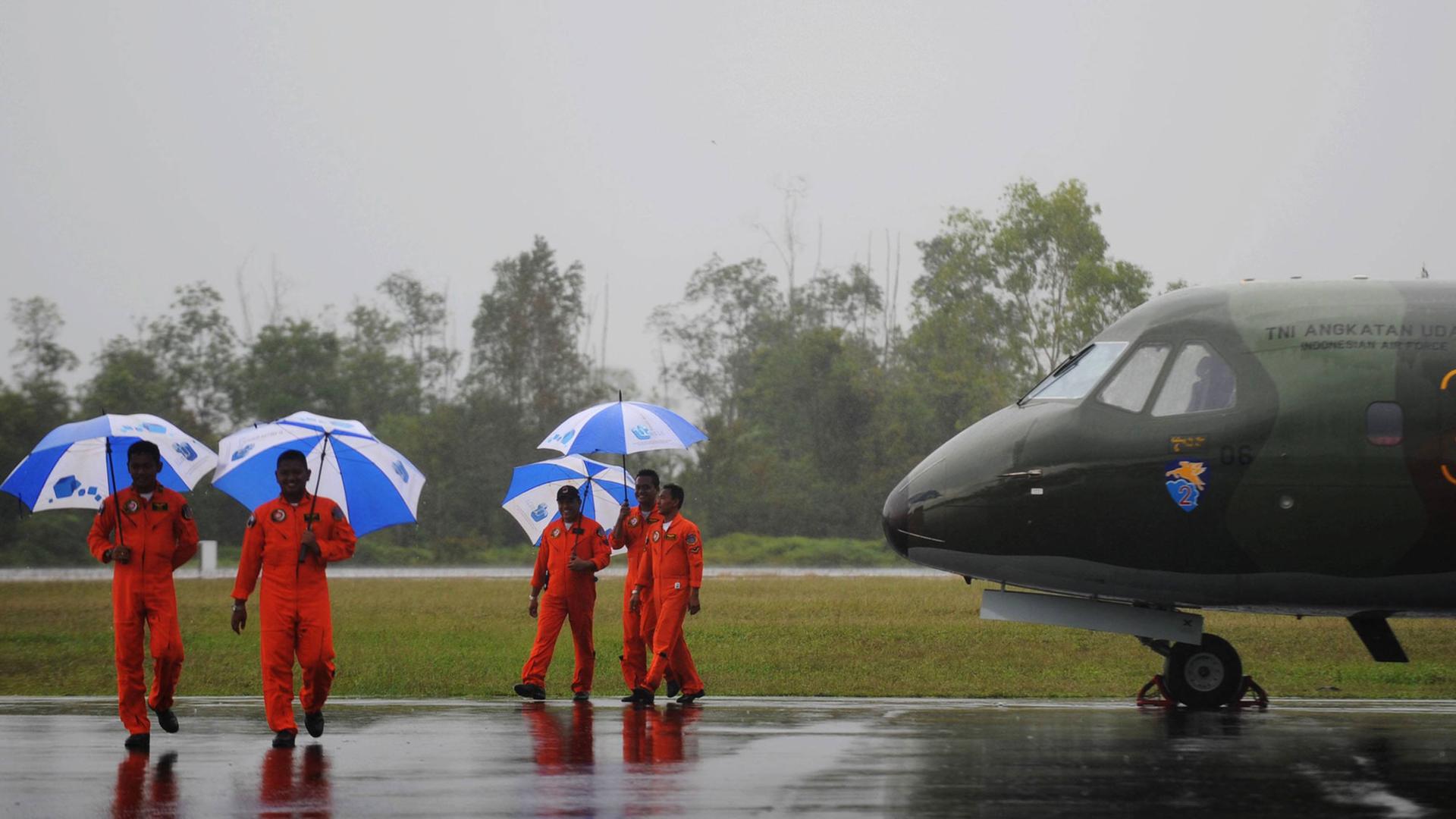 Vier Piloten der indonesischen Luftwaffe laufen mit Regenschirmen an einem Militärjet auf dem Rollfeld eines Flughafens entlang.