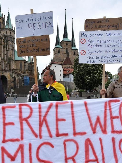 Demonstranten stehen auf dem Domplatz in Erfurt (Thüringen) bei einer Kundgebung der Alternative für Deutschland (AfD) gegen die Asyl- und Integrationspolitik von Bundes- und Landesregierung mit einem Banner mit der Aufschrift: "Merkel weg Amis raus".