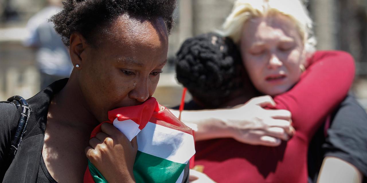 Eine Frau weint in eine Südafrika-Flagge, dahinter umarmen sich zwei weitere Frauen.