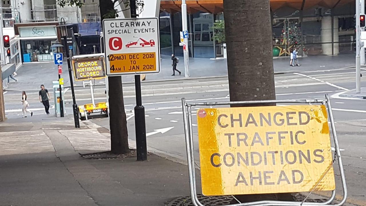 Ein gelbes Schild mit einem Verkehrshinweis lehnt am Baum neben einer abschüssigen Straße.