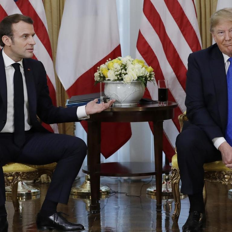 US-Präsident Donald Trump und Frankreichs Staatschef Emmanuel Macron sitzen nebeneinander. Macron gestikuliert und Trump schaut ratlos.