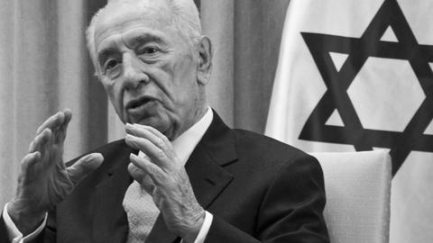 Ein alter Mann gestikuliert und spricht vor der Flagge Israels.