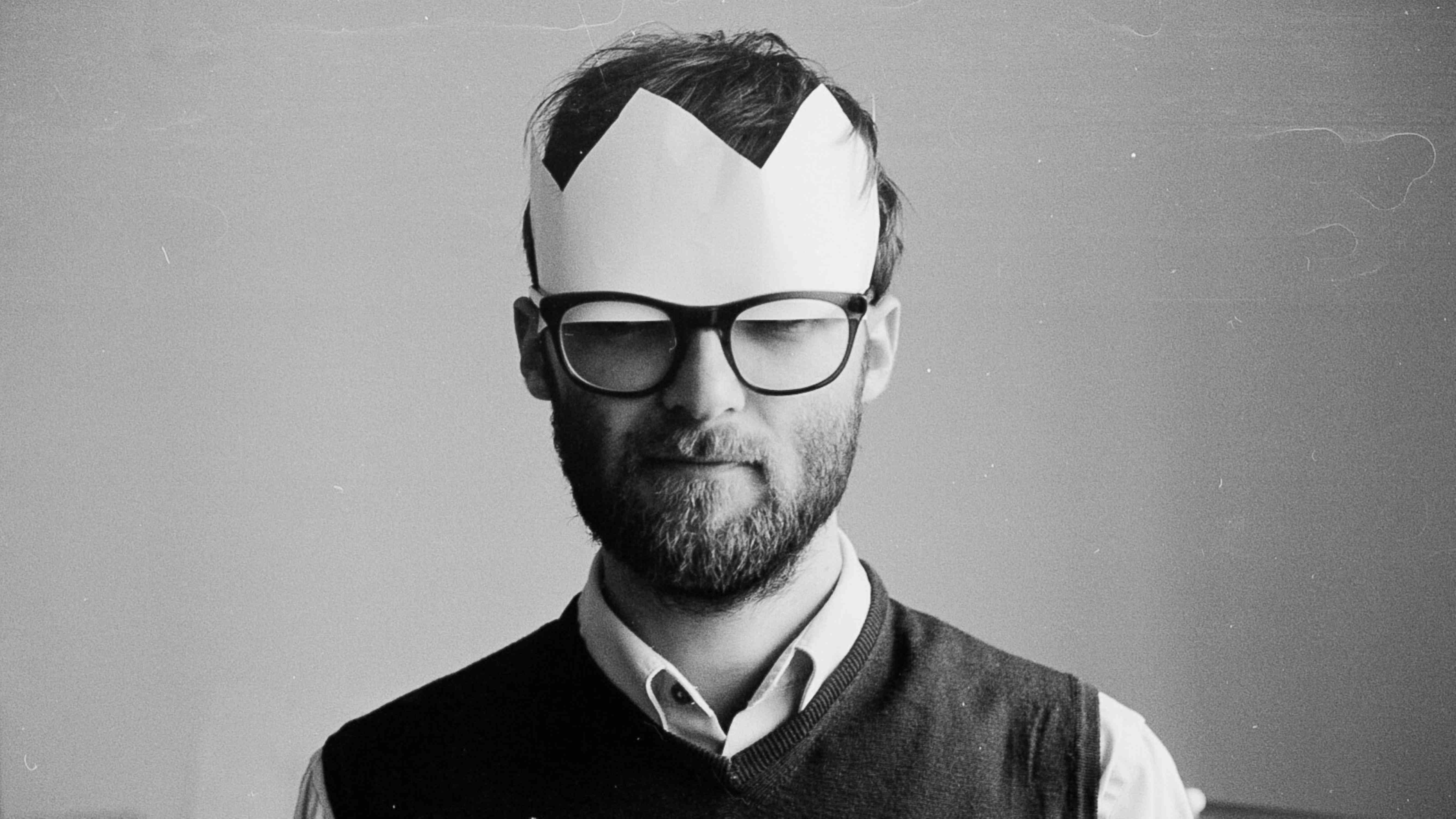 Ein schwarz-weiß-Foto mit einem Mann, der eine Pappkrone und eine große Brille trägt.