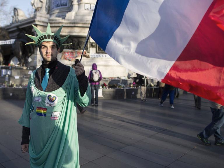 Ein Mann ist verkleidet als Freiheitsstatue und hält die französische Flagge in der Hand - er nimmt am Trauermarsch wegen des Anschlags gegen die Redaktion der Satirezeitschrift "Charlie Hebdo" in Paris am 11.01.2014 teil