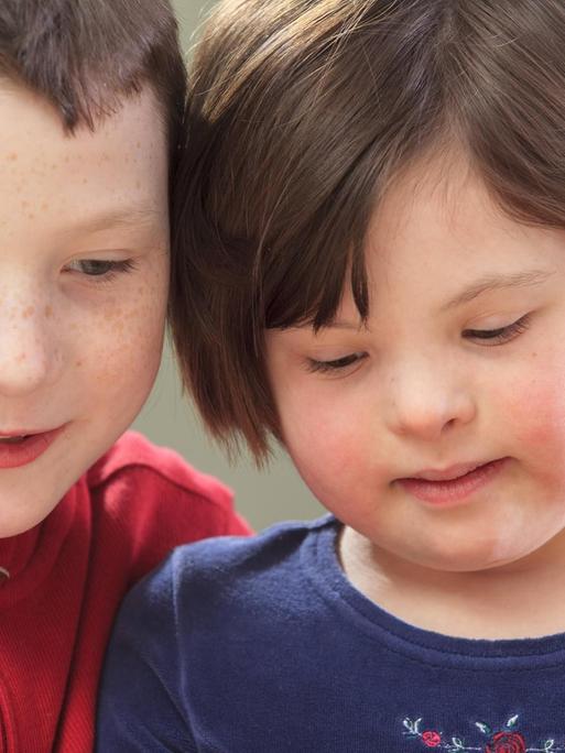 Eine Junge sitzt neben seiner jungen Schwester, die das Downsyndrom hat.