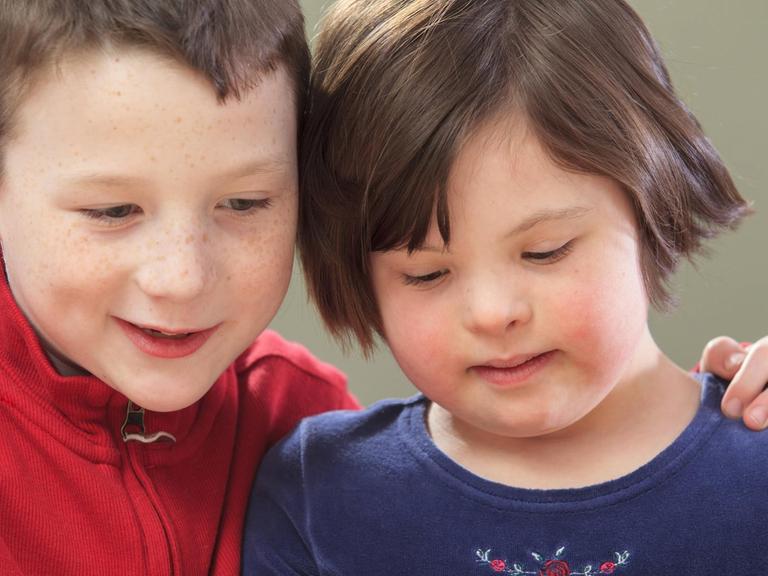 Eine Junge sitzt neben seiner jungen Schwester, die das Downsyndrom hat.