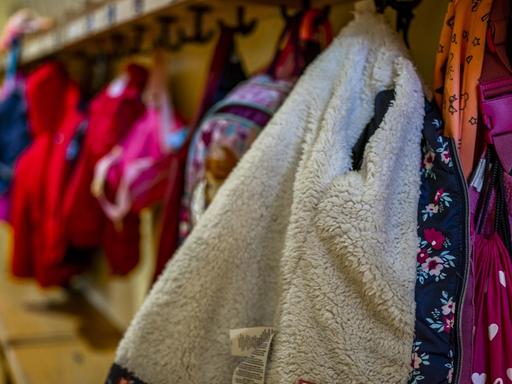 An einer Garderobe in einem Kindergarten hängen Jacken und Rucksäcke von Kindern.