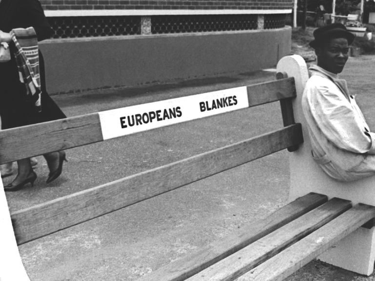 Ein junger schwarzer Mann sitzt in Durban auf der Seitenlehne einer Bank, die ausschließlich für Weiße reserviert ist, aufgenommen am 21.12.1962.