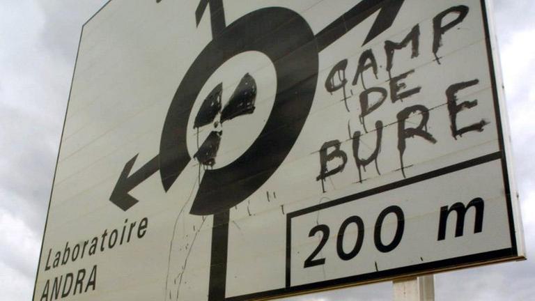 Ein Verkehrsschild, auf das jemand ein Atomkraftzeichen mit dem Hinweis "Camp De Bure" geschrieben hat.