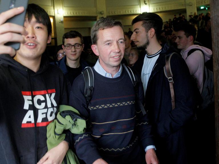 Bernd Lucke drängt sich nach seiner verhinderten Vorlesung aus dem Saal. Neben ihm ein Demonstrant in einem Pullover mit der Aufschrift "FCK AFD".
