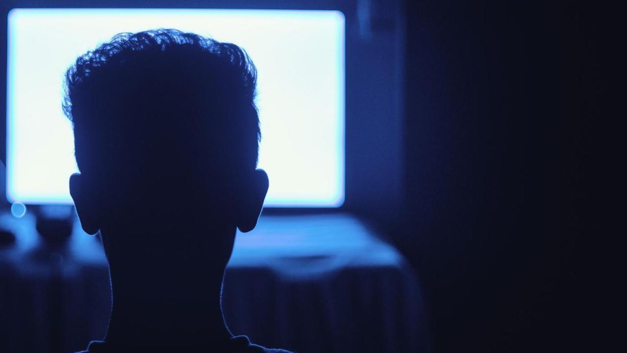Ein Mann sitzt in einem dunklen Raum vor einem hell erleuchtenden Monitor. Ein Mann sitzt in einem dunklen Raum vor einem hell erleuchtenden Monitor.