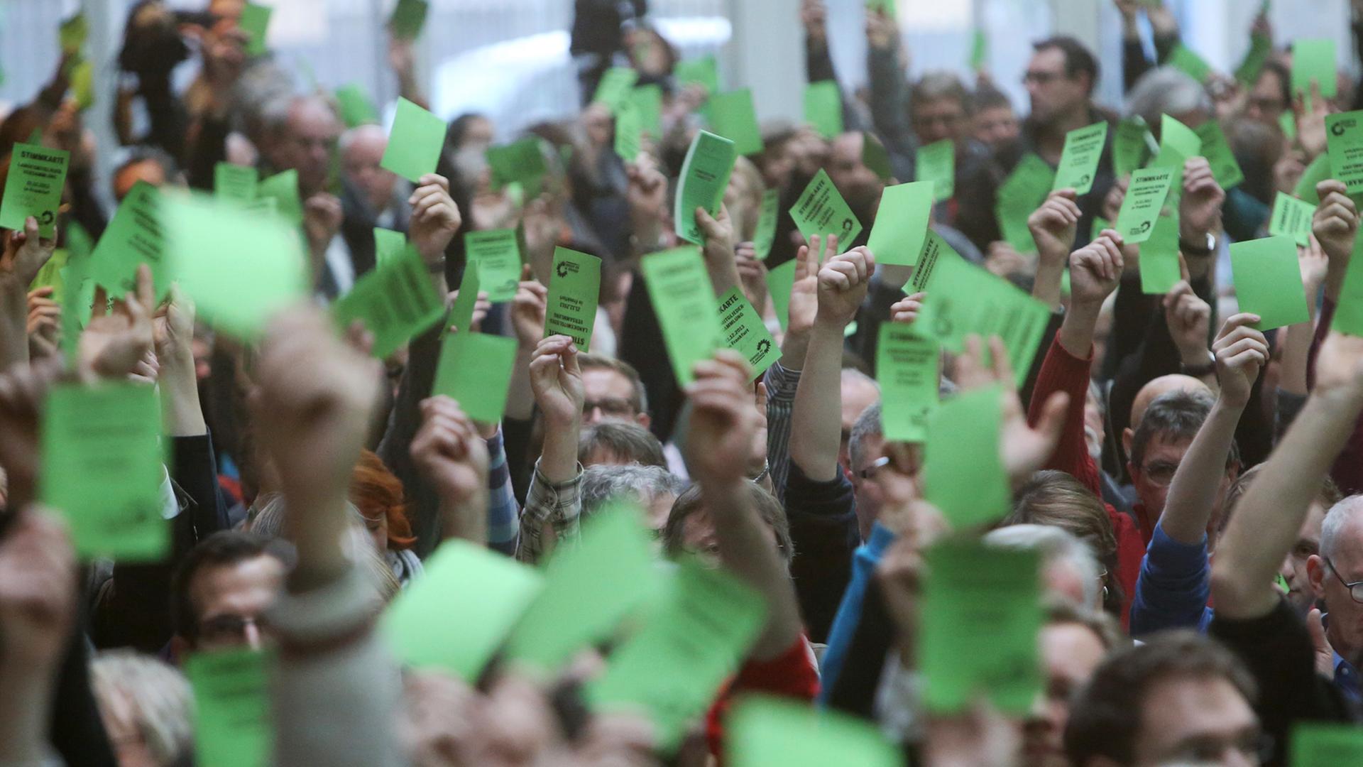 Mitglieder der Grünen halten auf einer Landesmitgliederversammlung grüne Stimmkarten in die Luft.
