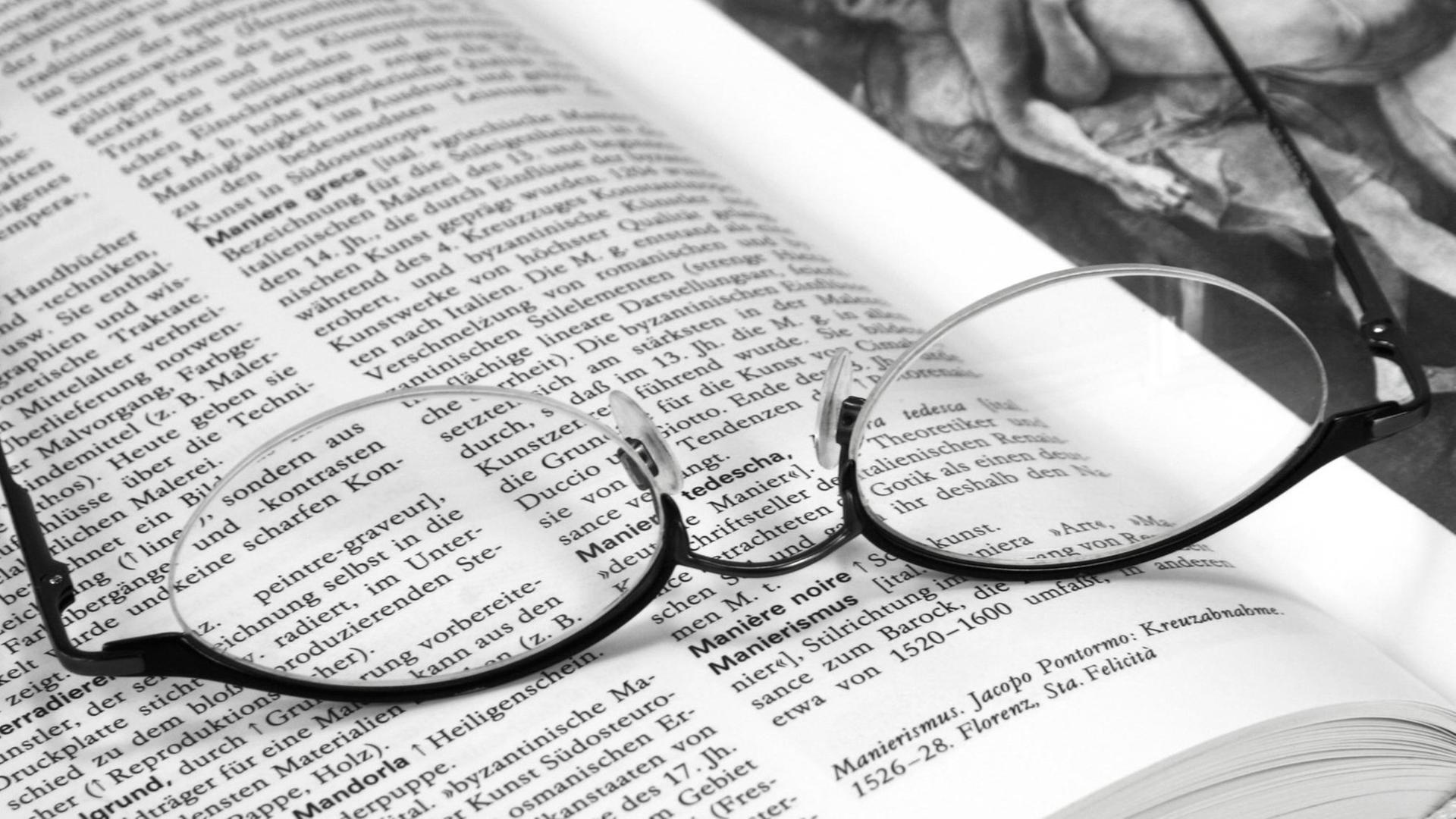 Eine Brille liegt auf den aufgeschlagenen Seiten eines Wörterbuchs
