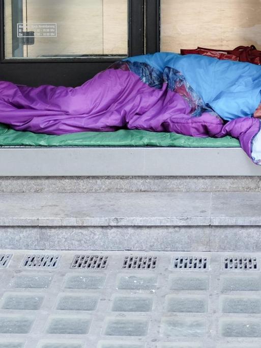 In einem Hauseingang in Berlin schläft ein Obdachloser in einem Schlafsack.