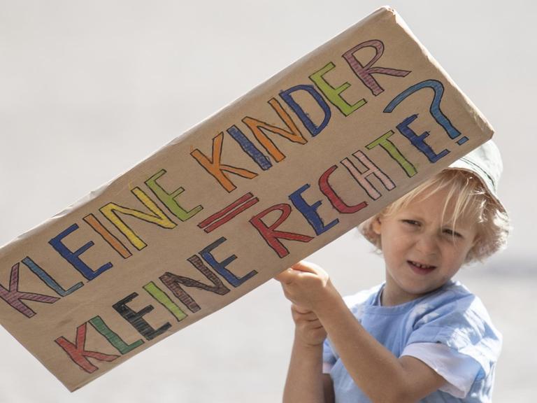 Ein Kind hält ein Plakat mit der Aufschrift "Kleine Kinder, Kleine Rechte?" in den Händen.