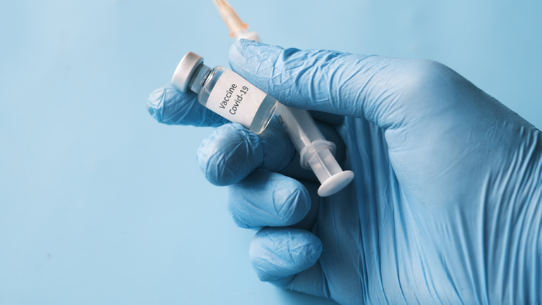 Eine Hand in medizinischem Handschuh hält Spritze und Corona-Impfstoff