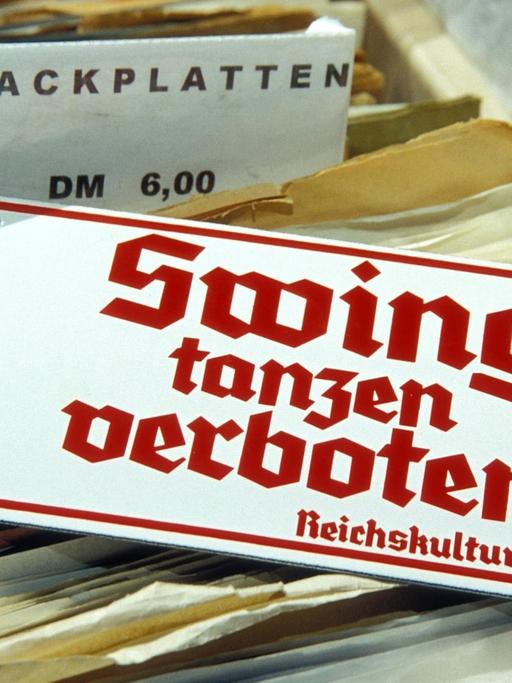Ein Schild mit der Aufschrift "Swing tanzen verboten - Reichskulturkammer" liegt auf Schellackplatten auf einem Flohmarkt
