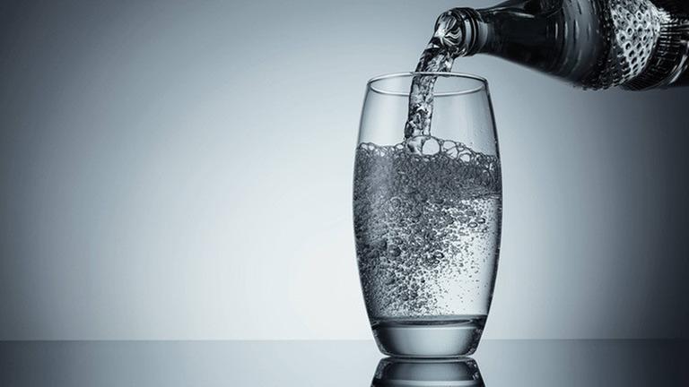 Wasser wird aus der Flasche in ein Glas eingeschenkt