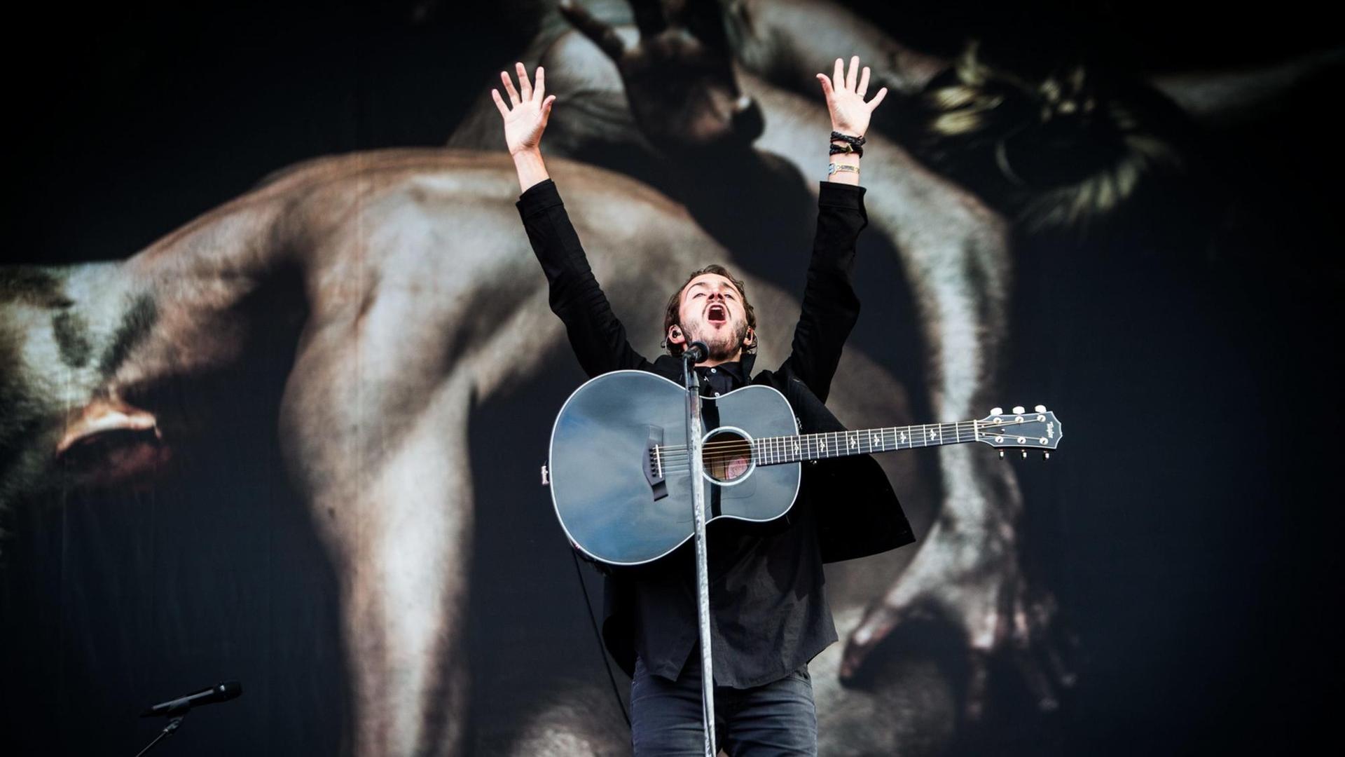 Tom Smith steht singend auf der Bühne und reißt die Hände in die Höhe.