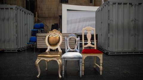 Drei Requisiten-Stühle stehen nebeneinander im Opernhaus des Theaters Magdeburg hinter der Bühne. Im Hintergrund sind Container zu sehen.