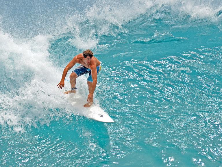 Ein Surfer auf einer Welle vor dem Waikiki Beach.