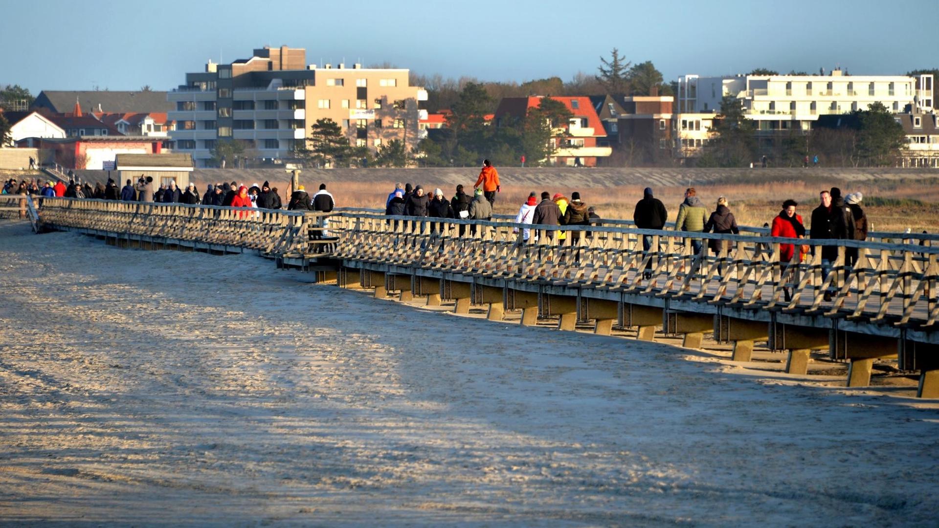 Touristen gehen über die Seebrücke am Strand in Sankt Peter-Ording.