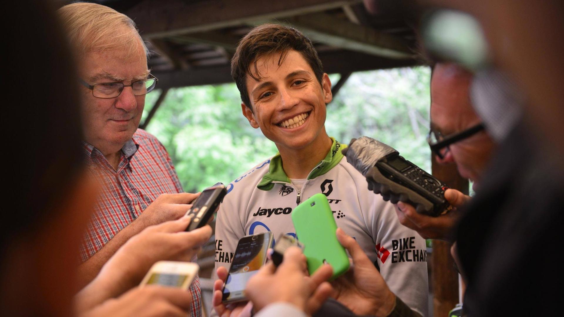 Der kolumbische Radsportler Esteban Chaves, umringt von Reportern, lächelt in die Kamera.