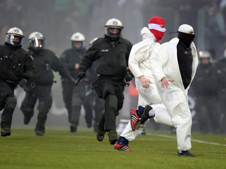 Im Borussia-Park in Mönchengladbach (Nordrhein-Westfalen) versuchen Polizisten, Kölner Fans auf dem Platz einzufangen.