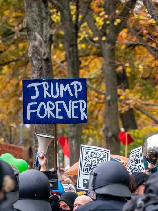 Nicht genehmigte Demonstration der Querdenken-Bewegung am. 18. November 2020 in Berlin. Vor einer herbstlichen Kulisse halten Demonstranten ein Schild "Trump forever" in die Höhe.