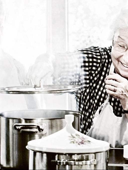 Zwei ältere Frauen stehen in einer hellen Küche und kochen fröhlich.