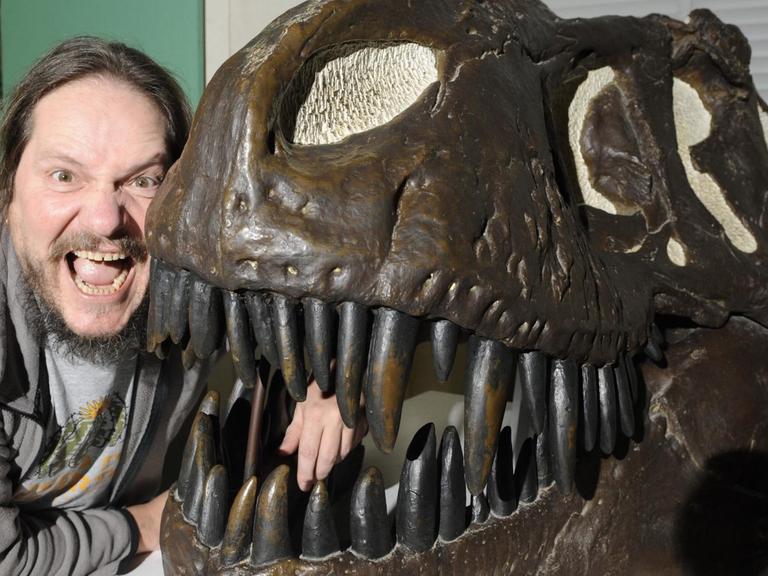 Saurierforscher Eberhard "Dino" Frey mit weit aufgerissenem Mund neben einem Schädelabguss eines Tyrannosaurus rex.