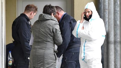Zwei Polizisten, eine Frau in Zivil und eine Mitarbeiterin der Spurensicherung in weißem Schutzoverall stehen vor einem Appartment.