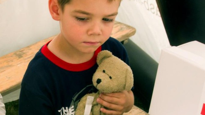 Zu sehen ist ein Junge mit seinem Teddy auf dem Arm