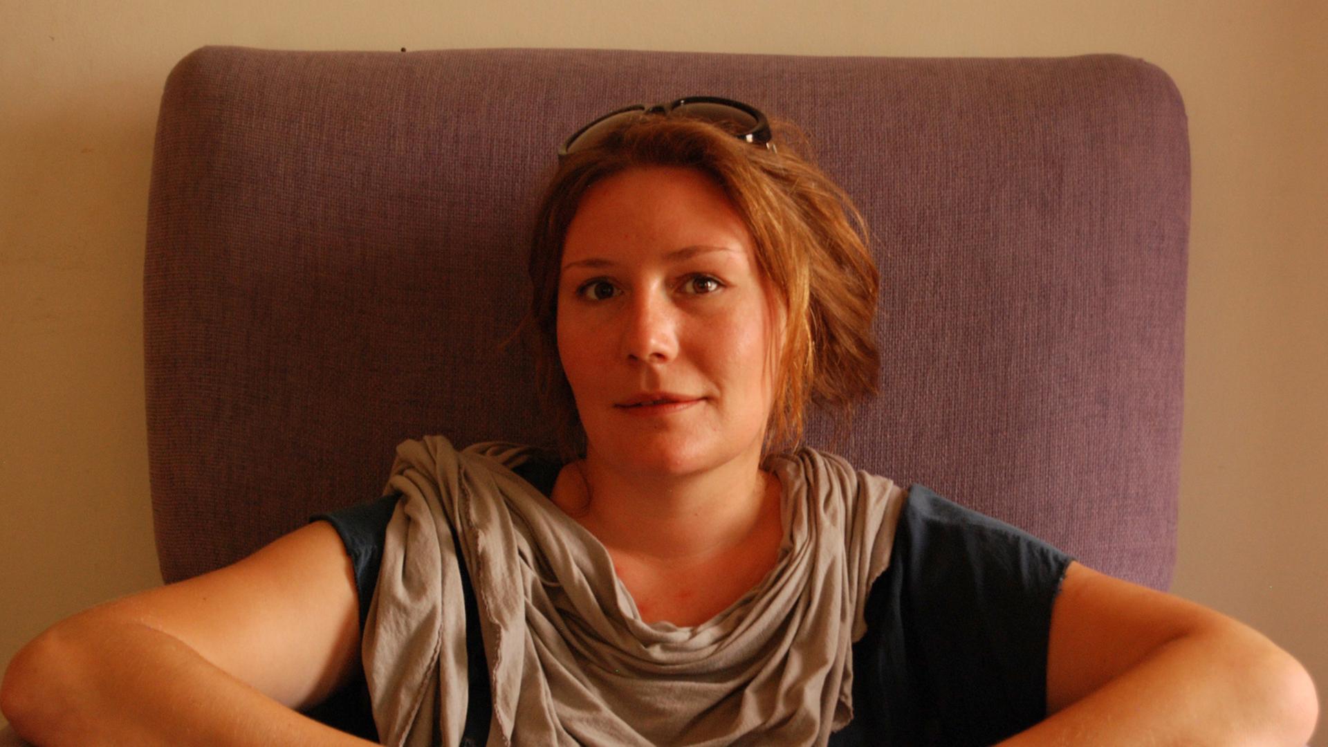 Die Autorin Noemi Schneider sitzt in einem Sessel und hält ein kleines Glas in der Hand.