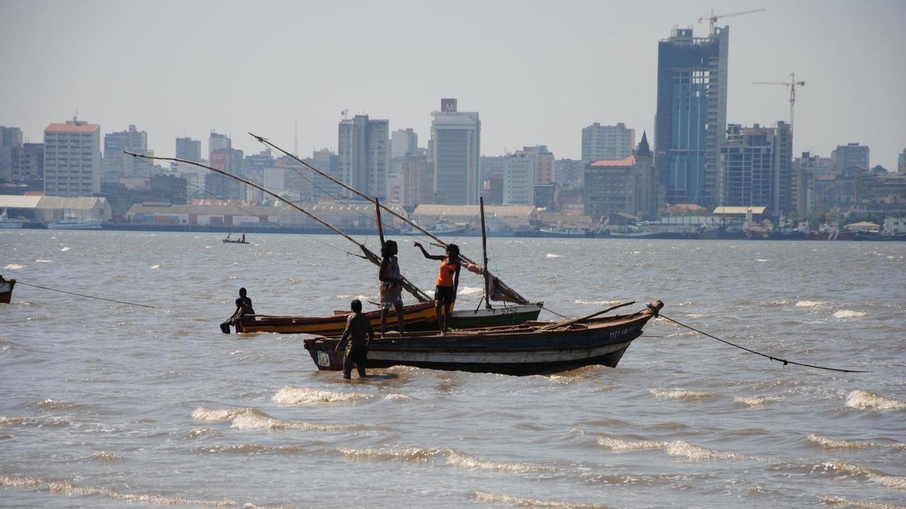Fischer auf dem Meer mit einfachen Booten, im Hintergrund Silhouette Maputops mit Hochhäusern