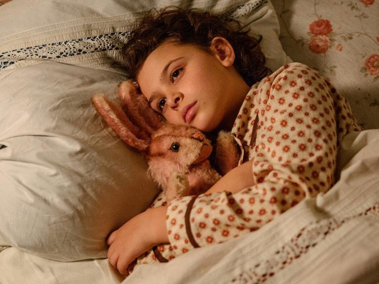 Filmstill aus dem neuen Film: "Als Hitler das rosa Kaninchen stahl", die Hauptdarstellerin Riva Krymalowski liegt mit einem Stoffhasen im Arm im Bett.