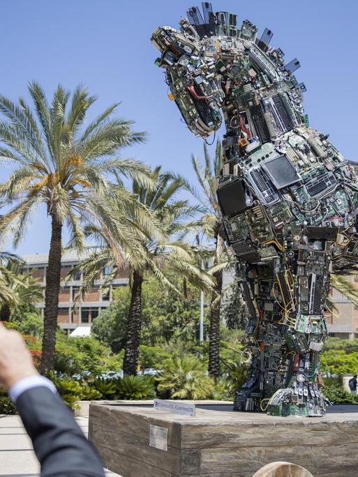 Ein Mann fotografiert die Skulptur eines Trojanischen Pferdes, zusammengesetzt aus mit Malware infizierten Computerteilen.