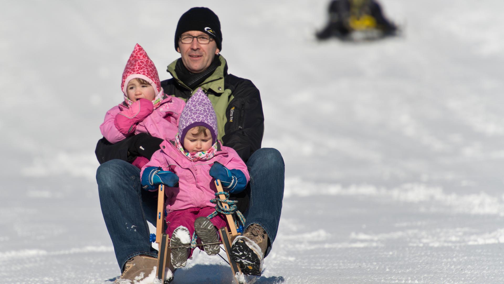 Ein Vater fährt auf dem Schauinsland bei Hofsgrund (Baden-Württemberg) mit den Zwilllingen Sophia und Ann auf dem Schlitten durch den Schnee.