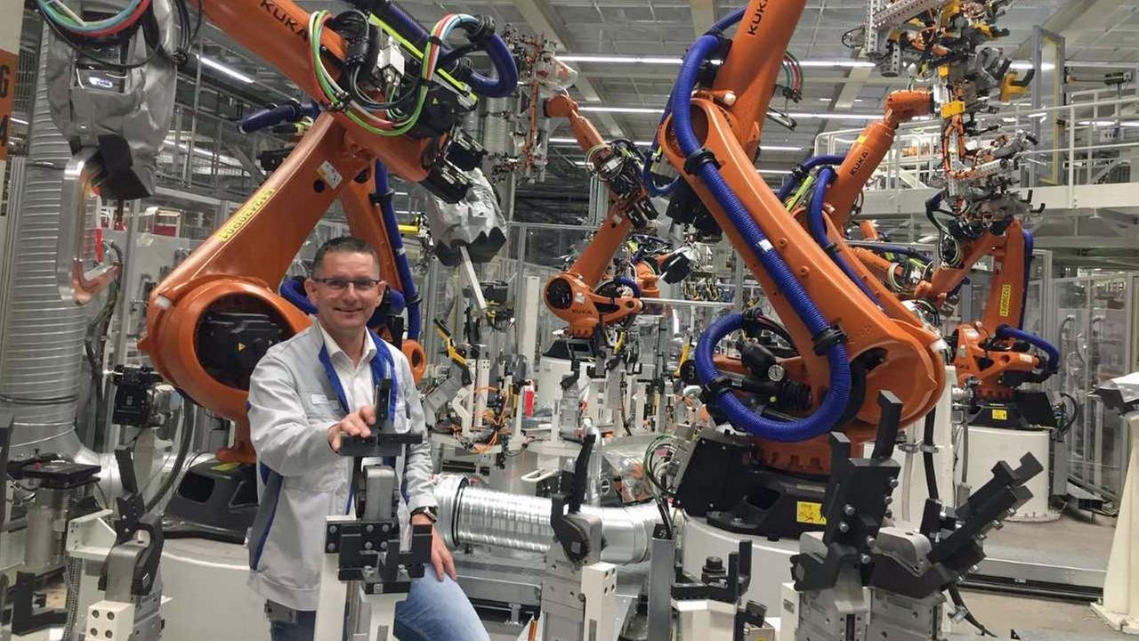 In einer Fertigungshalle des VW-Werks Zwickau steht Heiko Rösch im weißen Kittel umgeben von orangefarbenen Maschinen.