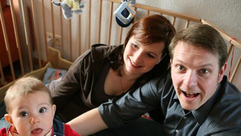 Vater, Mutter, Kind sitzen in einem Laufstall