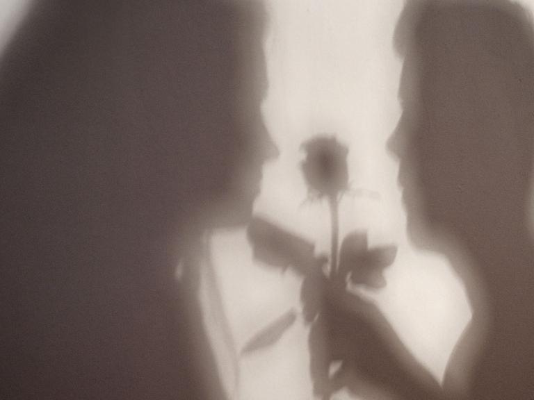 Der Schatten einer Frau und eines Mannes, der ihr eine Rose übergibt, sind an eine Wand geworfen.
