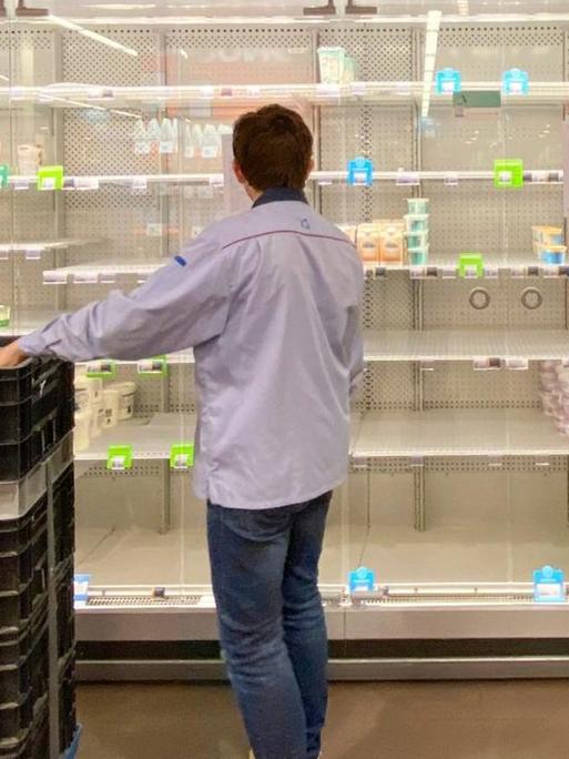 Ein junger Mann räumt ein halbleeres Supermarktregal ein.