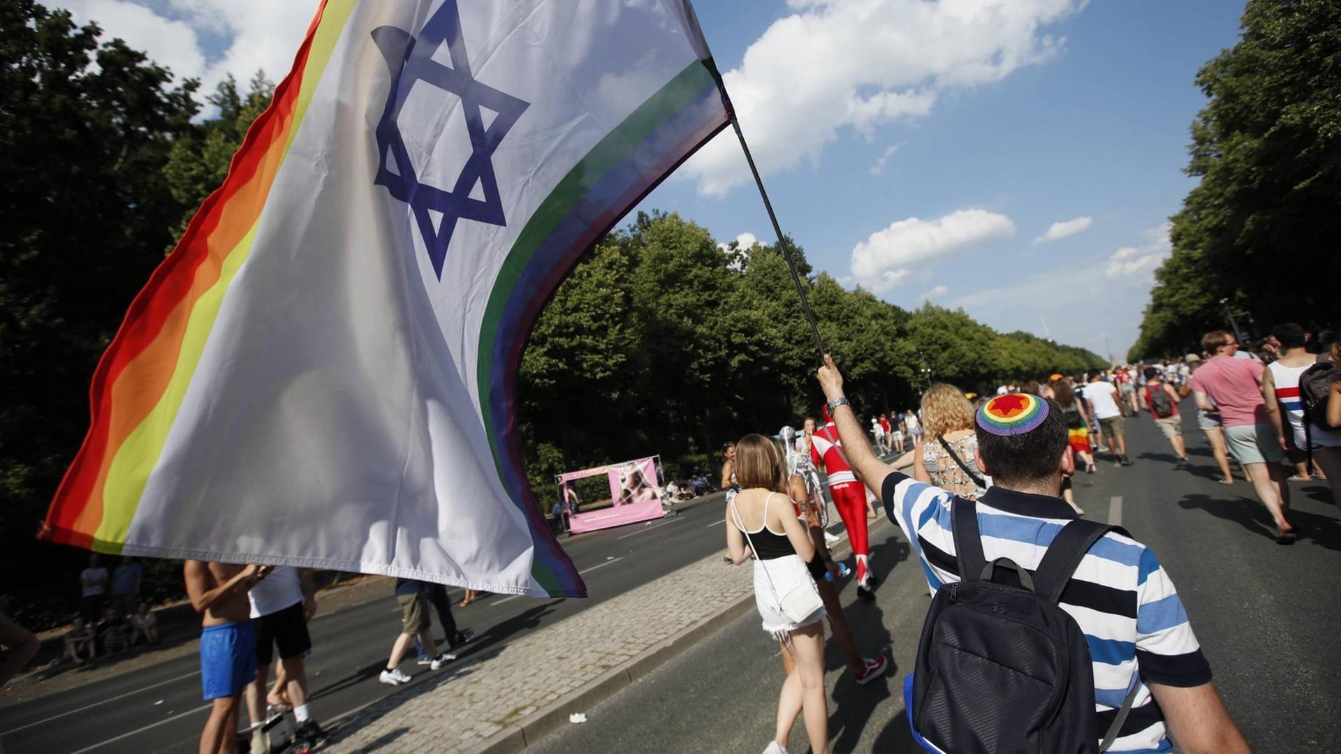 Jüdischer Teilnehmer auf dem CSD-Berlin mit regenbogenfarbener Kippa und Fahne